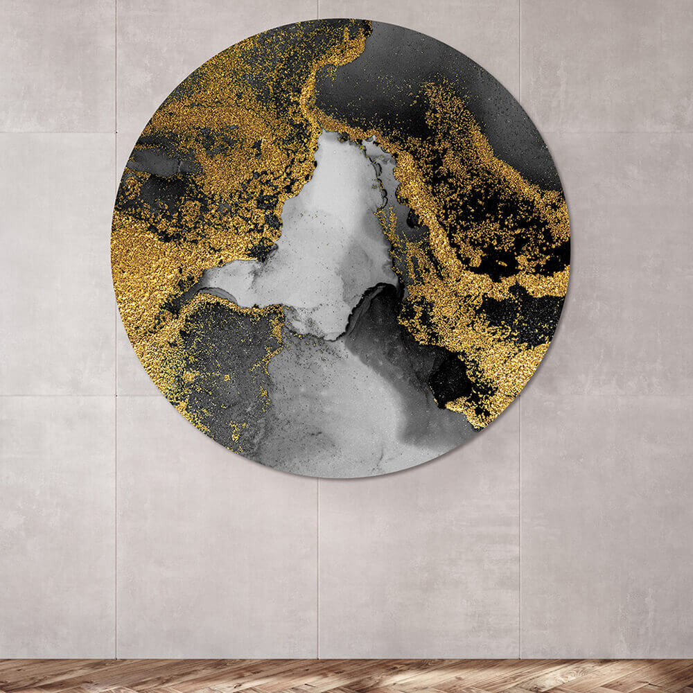 Rundes Akustikbild an einer Wand hängend mit einem abstrakten Motiv. Goldene DFarbe mit schwarz grauer Farbe verschwimmt miteinander. Das Akustikbild hängt an einer grauen steinwand.